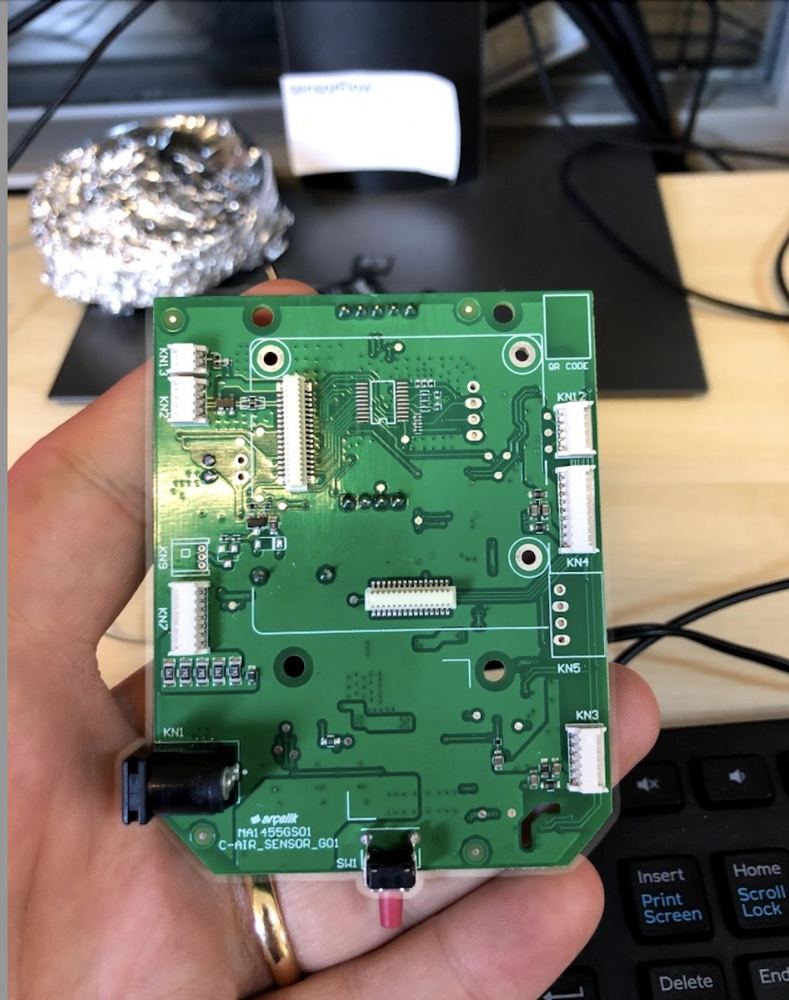 A hand holding a custom air-sensor printed circuit board.